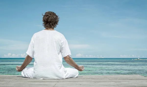 Genç adam sahilde meditasyon yapıyor.