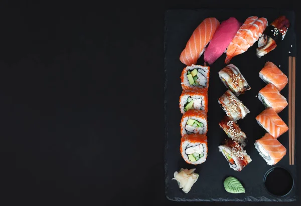 Sushi rolls on black slate plate. Set for one person with chopsticks, ginger, soy, top view, copy space. Japanese cuisine.