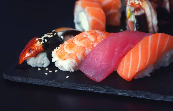 Japon nigiri suşisi ve unagi, bataklık, ton balığı ve somon balıklı siyah taş tabakta rulo. 