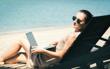 Genç güzel kız kumsalda dizüstü bilgisayar kullanarak iletişim kuruyor.