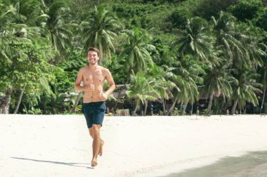 Plajda palmiye ağaçlarının arkasında koşan çekici bir genç.