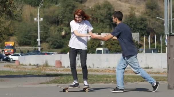 Τύπος διδάσκει μια κοπέλα πώς να οδηγούν ένα skateboard στο πάρκο — Αρχείο Βίντεο