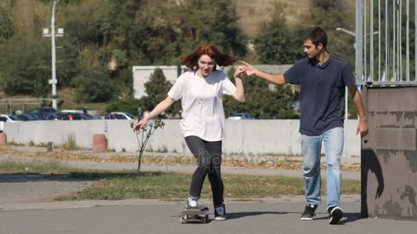 Guy enseña a una chica a montar un monopatín — Vídeo de stock