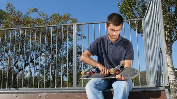 Uomo che ripara uno skateboard, rampa sullo sfondo . — Video Stock