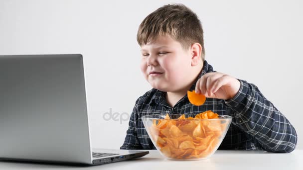 Giovane ragazzo grasso mangia patatine fritte e e guardare cartoni animati su un computer portatile 50 fps — Video Stock