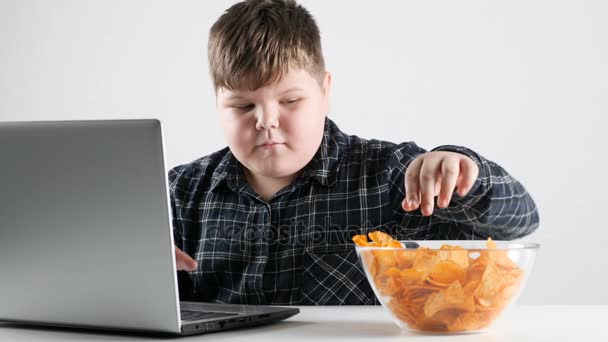 年轻的胖男孩吃薯条和在笔记本电脑上玩 50 fps — 图库视频影像