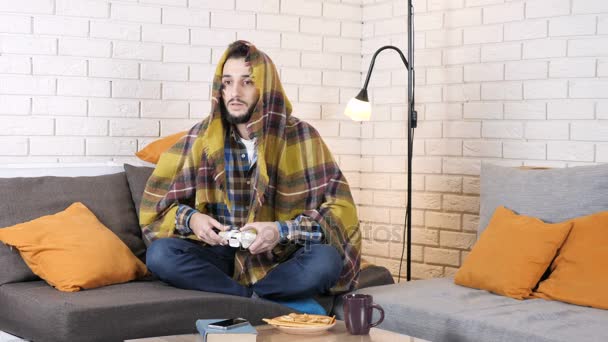 白人の男は、毛布の下のソファに横たわっていると 50 fps を失うコンソール ゲームをプレイ — ストック動画