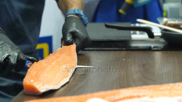 Manos de hombre con guantes negros cortan la piel de los filetes de pescado — Vídeo de stock
