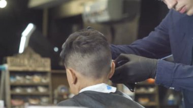 Kuaför siyah eldiven dikkatle ense ve Asyalı bir çocuk bir kuaför dükkanında viski tıraş, geri 60 fps görüntüleme