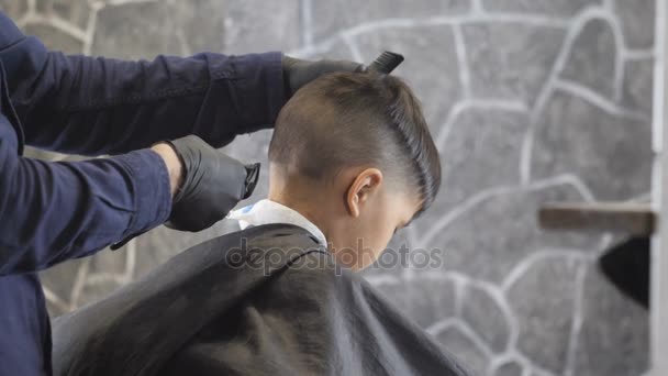 Friseur in schwarzen Handschuhen rasiert einem asiatischen Kind in einem Friseurladen vorsichtig den Nacken, Nahaufnahme 60 fps — Stockvideo