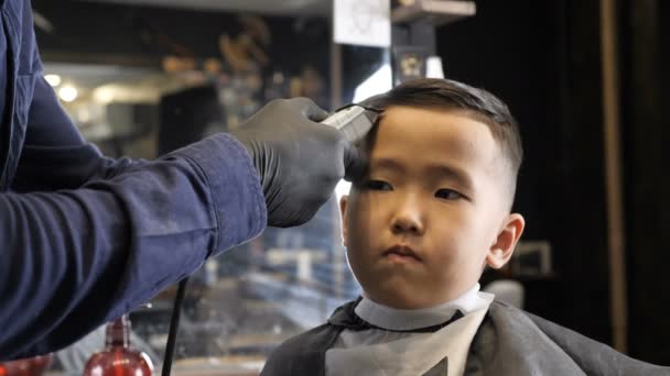 Peluquero en guantes negros afeita suavemente flequillo Niño asiático 60 fps — Vídeos de Stock