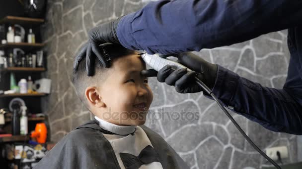 Fryzjer w czarne rękawiczki delikatnie goli grzywka szczęśliwy Asian dziecko 60 fps — Wideo stockowe