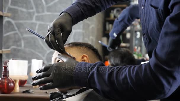 Barber in black gloves neatly shaves whiskey with a straight razor to an Asian kid 60 fps — Stock Video