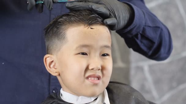 Barber in black gloves cuts hair on the crown of an Asian child, the boy is  in shock 60 fps — Stock Video ©  #176270808