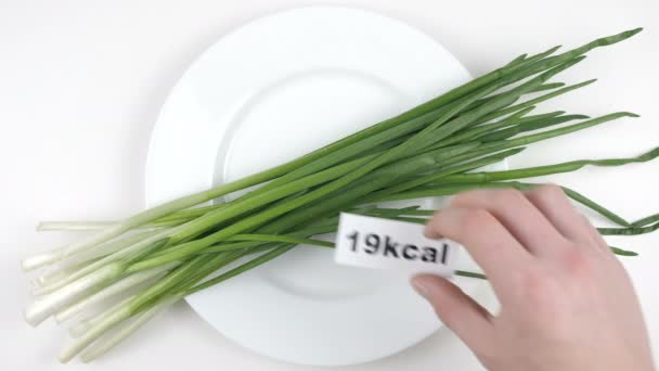 Cantidad de calorías en cebolla verde, mano masculina pone un plato con el número de calorías en una cebolla verde, tiro superior — Vídeos de Stock