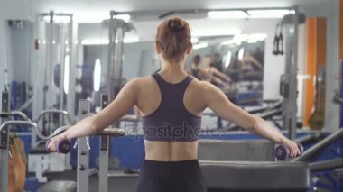 Spor genç kız tarafı dumbbell yapıyor bir spor salonunda spor bankta otururken yükseltir. Arka taraf görüntülemek 60 fps kadar yakın
