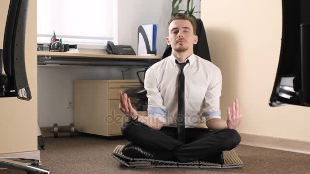 Jovem em um terno meditando em uma pose de lótus no meio de um escritório 60 fps — Vídeo de Stock