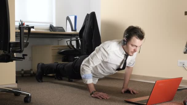 Jovem de terno e usando fones de ouvido push-ups na frente do laptop 60 fps — Vídeo de Stock