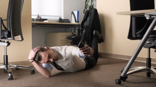 Молодой человек делает селфи, лежа на полу в центре офиса. 60 кадров в секунду — стоковое видео