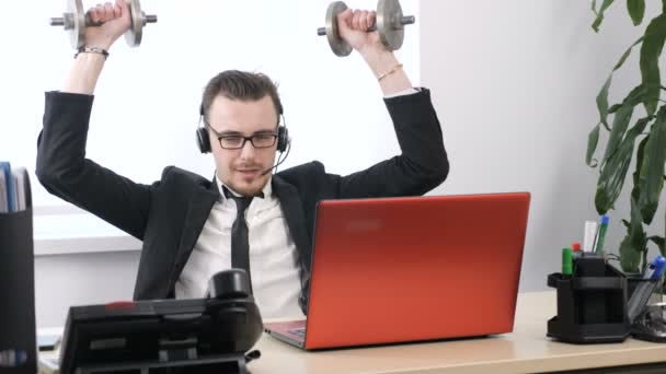 Молодий чоловік у костюмі працює в офісі і займається вправами для плечей з гантелі. 60 к/с — стокове відео