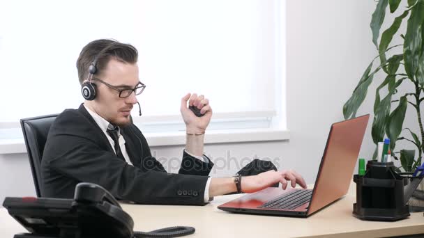 Egy fiatal srác, egy öltöny és szemüveg működik egy laptop és squeezes kézi expander 60 fps — Stock videók