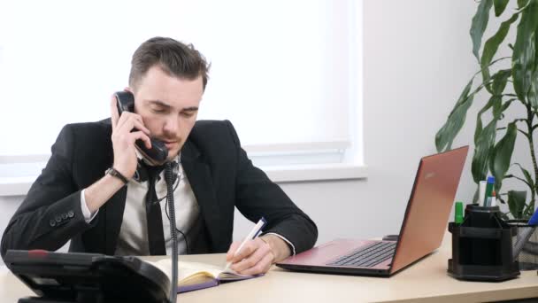Bir takım elbiseli genç adam telefonda konuşuyor ve bir not defterinde yazıyor 60 fps — Stok video