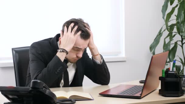 Desperate young businessman sitting at desk in office and grabbing his head 60 fps — Stock Video