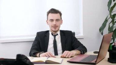 Takım elbiseli genç işadamı ofisinde oturan ve başparmak gösterilmesini oturum 60 fps