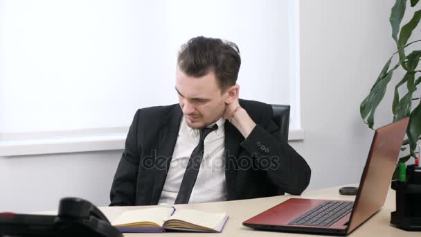 Joven hombre de negocios en traje sentado en la oficina, cansado, amasando su cuello 60 fps — Vídeo de stock