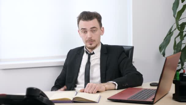 Jonge zakenman in pak zitten in kantoor en tonen van call me ondertekenen. 60 fps — Stockvideo