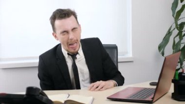 Office ve sopalarla dilini dışarı, yapar komik yüzler 60 fps oturan takım elbiseli genç işadamı