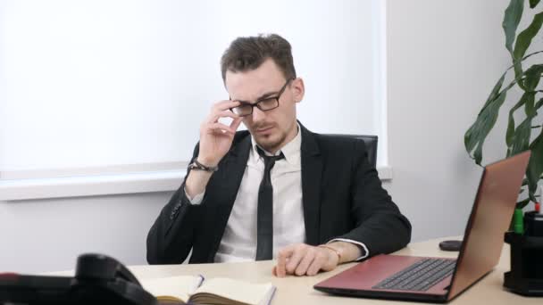 Jonge moe zakenman in een pak zijn bril opstijgt en sluit zijn ogen met zijn handen van 60 beelden per seconde — Stockvideo