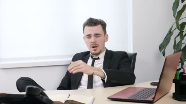 Молодий втомлений бізнесмен в костюмі сидить в офісі і позіхає 60 кадрів в секунду — стокове відео