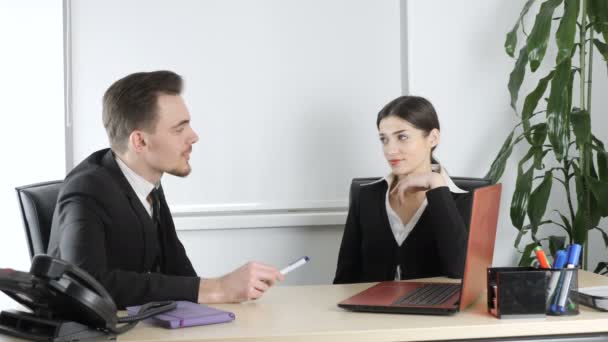 Молодий чоловік і жінка в костюмах розмовляють в офісі, чоловік відволікається на телефонну розмову. Офісні працівники, бізнес 60 к/с — стокове відео