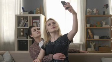 İki genç, güzel kız kanepede oturan ve selfies, lezbiyenler, Lgbt, sarışın, esmer yapma 60 fps