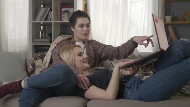 Mladá blond žena leží na klíně bruneta a dívají se na vtipné video o laptop, přátelé, lesbičky, volný čas, odpočinek, pár. 60 snímků za sekundu — Stock video