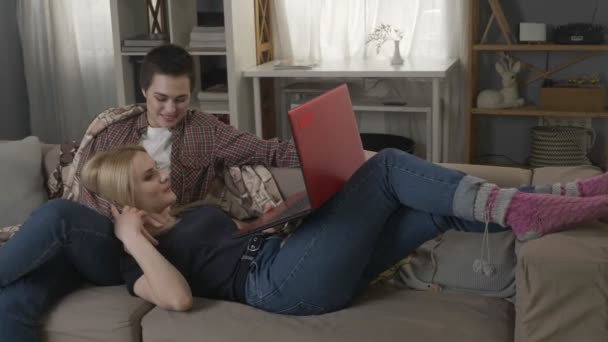 Ung blond kvinna ligger i knät på en brunett och använda röd laptop, mys, kramar, 60 fps — Stockvideo