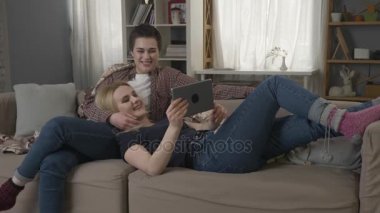 Lezbiyen çift kanepede oturan ve tablet komik film izlerken, yavaşça onu okşayarak kısa saçlı bir kız saç ortakları 60 fps
