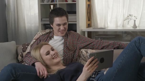Lesbický pár odpočívá na gauči, pomocí tabletu a smějící se, mladá rodina, kostkované, útulné 60 fps — Stock video