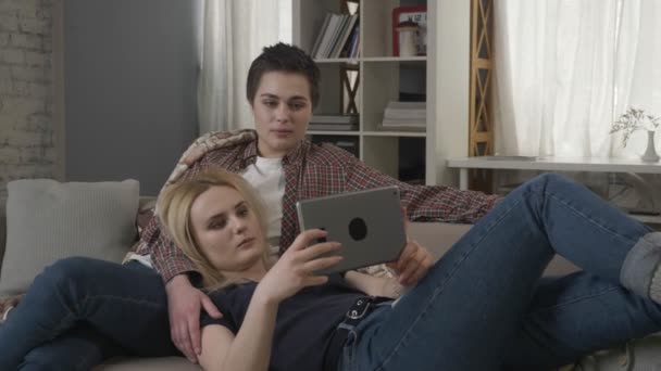 Лесбиянки отдыхают на диване, используя планшетный компьютер, говорят, показывая знак нет, качая головой 60 кадров в секунду — стоковое видео