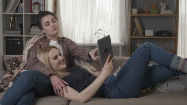 Lesbisches Paar ruht sich auf der Couch aus, benutzt Tablet-Computer, spricht, Familienidylle 60 fps — Stockvideo