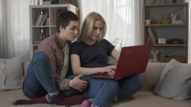 İki genç lezbiyen kızlar bir bilgisayar kullanılarak koltukta oturan sarışın kötü niyetle alışveriş online, internet, kaydırma laptop kapanır, 60 fps kavga
