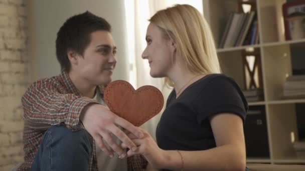Две молодые лесбиянки мило смотрят друг на друга, держа в руке знак сердца, улыбаются, смеются 60 кадров в секунду — стоковое видео