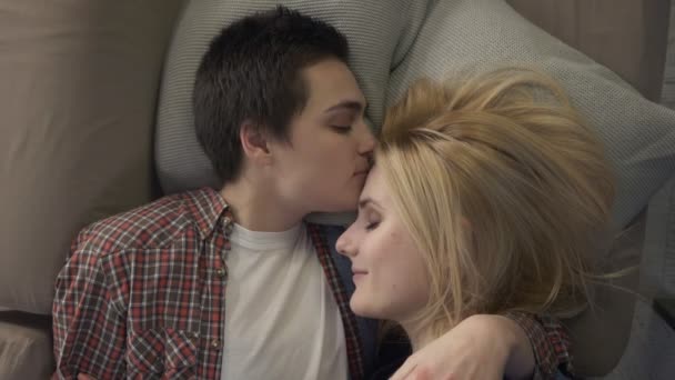 Két fiatal leszbikus lányok ágyon, egy rövid hajú lány csók élettársa, a homlokán, az LMBT járműcsalád-koncepció, hogy aludni, pihenni 60 fps — Stock videók