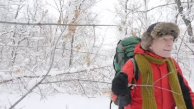 Yaşlı beyaz gülümseyen adam Hiking sopa ile karlı bir orman yoluyla girer. Ağaçlar ve karla kaplı ormanda kökleri kalın yoğun çalılık. Yürüyüş ve kavram seyahat 60 fps