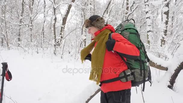 Anciano caucásico se quita la mochila y la pone en el suelo. Grueso matorral denso de árboles y raíces en el bosque cubierto de nieve. Concepto de caminata y parada 60 fps — Vídeo de stock