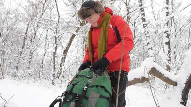 Äldre kaukasiska man avlägsnar vinterhandskar och kastar dem på golvet i en snötäckt skog. Tjocka täta snår av träd och rötter i i den snötyngda skogen. Vandra och resa concept 60 fps — Stockvideo