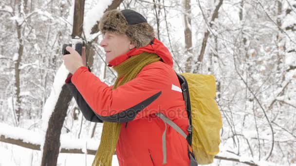 Ευρωπαϊκό ηλικιωμένος λήψη φωτογραφιών σε dslr φωτογραφική μηχανή σε ένα χιονισμένο δάσος. Παχύ πυκνό άλσος των δέντρων και τις ρίζες στην στο χιονισμένο δάσος. Πεζοπορία και ταξίδια έννοια 60 fps — Αρχείο Βίντεο