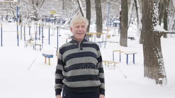 Ένας ηλικιωμένος Ευρωπαίου ανθρώπου κάνει ένα πρωί εξωτερική προθέρμανσης το χειμώνα, άσκηση για μια προθέρμανση του πίσω, κλίσεις προς τα εμπρός. Έννοια της υγιούς ζωής. 60 fps — Αρχείο Βίντεο