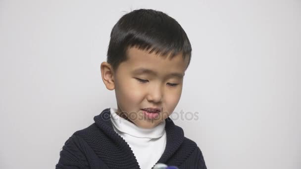 アジアの子供は手で洗濯粉ポッドを保持します。洗剤でカプセルを食べようとして、チャレンジ、インターネットのミームのさや洗濯洗剤。60 fps — ストック動画
